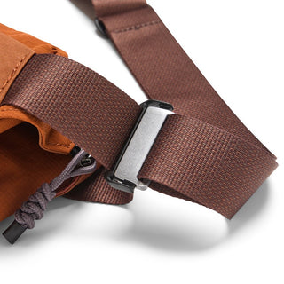 Bellroy Venture Sling 6L close-up of brown adjustable strap and metal buckle detail on orange fabric bag