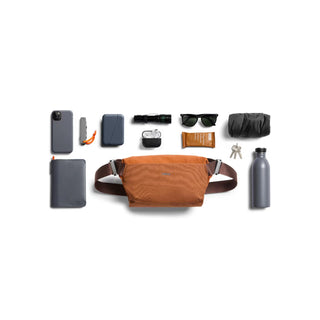 Bellroy Venture Sling 6L in rust color displayed with everyday carry items on white background