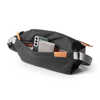 Bellroy Sling - 7L in black water-resistant fabric with leather accents and front zipper pocket open with items inside