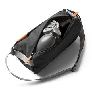 Bellroy Sling - 7L in black woven fabric with eco-leather accents, open showing water bottle and clothing inside