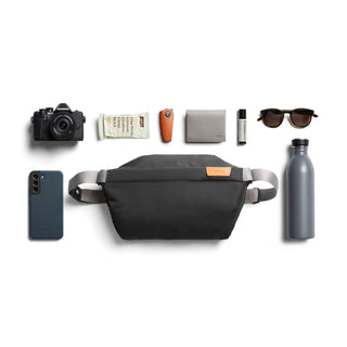 Bellroy Sling - 7L in black woven fabric with leather patch, shown with everyday carry essentials arranged around it