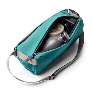 Bellroy Sling - 7L in teal fabric with adjustable strap, unzipped showing bottle and camera inside