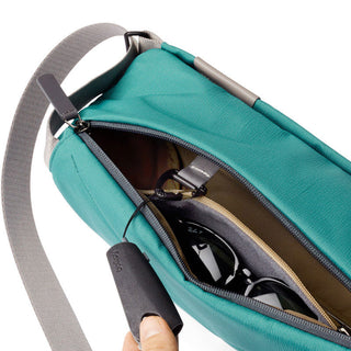 Bellroy Sling - 7L in teal woven fabric with grey strap showing sunglasses inside zipped main compartment