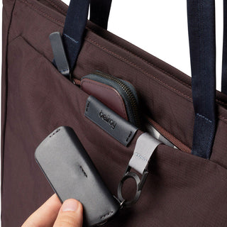 Bellroy Tokyo Tote Compact in brown woven fabric with front pocket holding accessories and hand pulling item