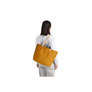 Bellroy Market Tote in mustard yellow recycled nylon carried over shoulder by person wearing grey outfit