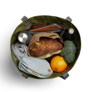 Bellroy Market Tote in olive green filled with groceries including bread, orange, broccoli, and personal items