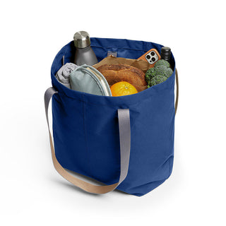Bellroy Market Tote in blue carrying groceries and accessories with sturdy beige handles