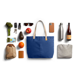 Bellroy Market Tote in navy blue recycled nylon with natural leather handles and daily essentials arranged around it