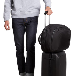 Bellroy Transit Backpack Plus in black woven fabric resting on a rolling suitcase handle