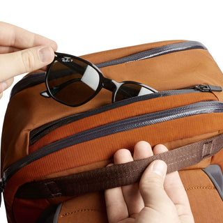 Bellroy Transit Workpack 20L in brown fabric with top handle and zipper pocket holding sunglasses