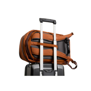 Bellroy Transit Workpack 26L in burnt orange with padded straps attached to suitcase handle