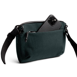 Bellroy Venture Travel Crossbody in dark green with front zipper pocket holding a smartphone