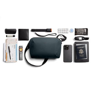 Bellroy Venture Travel Crossbody in black with smooth fabric and adjustable strap, surrounded by travel essentials