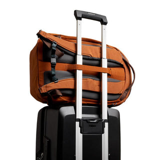 Bellroy Venture Ready Pack 20L in burnt orange attached to black suitcase handle showing padded back straps
