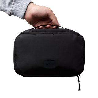 Bellroy Hanging Toiletry Kit in black recycled nylon held by hand with zipper and compact design