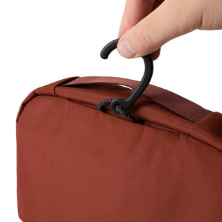 Bellroy Hanging Toiletry Kit in burnt orange fabric with sturdy black hanging hook held by hand
