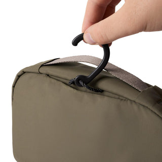 Bellroy Hanging Toiletry Kit in olive fabric with black hook held by hand against white background