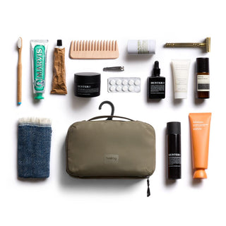 Bellroy Hanging Toiletry Kit in olive green fabric with a hanging hook and travel essentials arranged around it