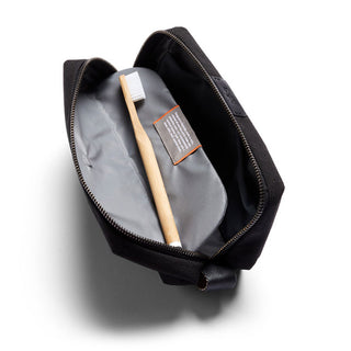 Bellroy Toiletry Kit open with gray interior lining and wooden toothbrush inside on white background