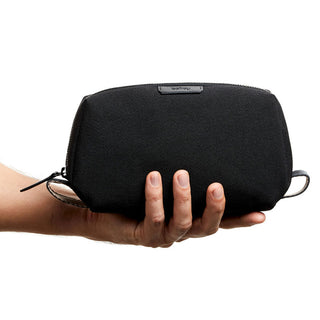 Bellroy Toiletry Kit in black recycled fabric held in hand showing compact, sleek design and textured finish
