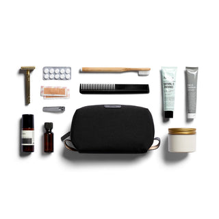 Bellroy Toiletry Kit in black fabric with travel-sized grooming essentials and accessories arranged around it