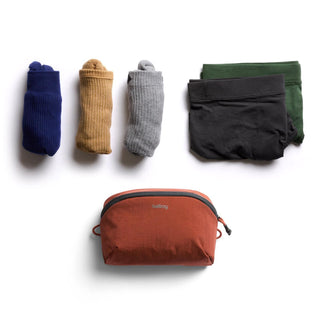 Bellroy Lite Packing Pouch 2L in rust with soft fabric and zipper, next to neatly folded socks and underwear