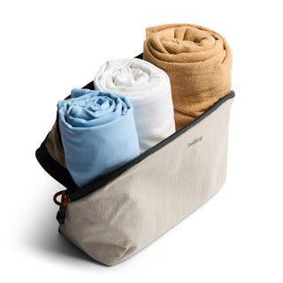 Bellroy Lite Packing Pouch 3L holding three rolled fabric items in beige recycled nylon pouch with zipper