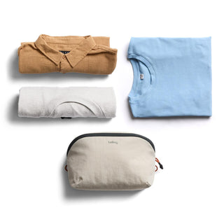 Bellroy Lite Packing Pouch 3L in light beige with smooth texture surrounded by folded casual shirts