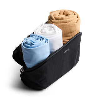 Bellroy Lite Packing Pouch 3L in black fabric holding three rolled towels in blue, white, and beige