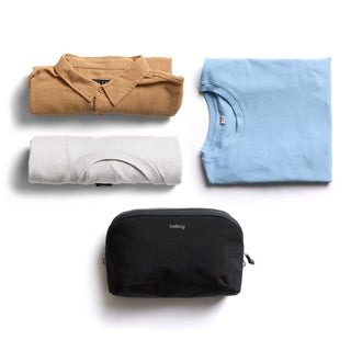Bellroy Lite Packing Pouch 3L in black nylon alongside folded clothes on white background