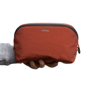Hand holding rust-colored Bellroy Lite Packing Pouch 3L made from recycled nylon fabric