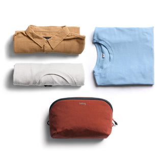Bellroy Lite Packing Pouch 3L in rust color beside folded casual clothes on white background