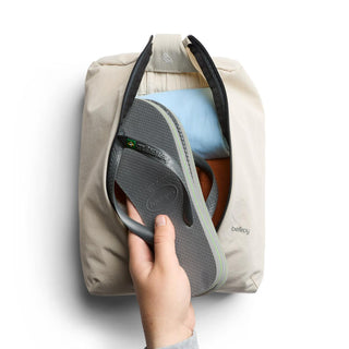 Bellroy Lite Packing Caddy 8L in beige fabric holding a gray flip flop and folded clothes inside