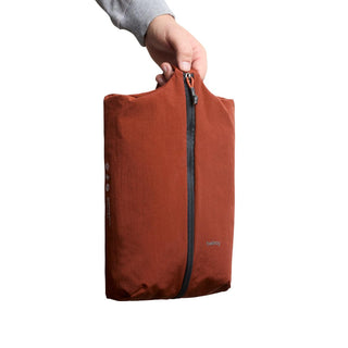 Bellroy Lite Packing Caddy 8L in rust color held by hand showing vertical zipper closure