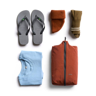 Bellroy Lite Packing Caddy 8L in rust color packed with casual clothing and sandals on white background