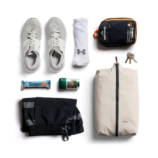 Bellroy Lite Packing Caddy 10L in beige with zipper, shown alongside travel essentials and workout gear