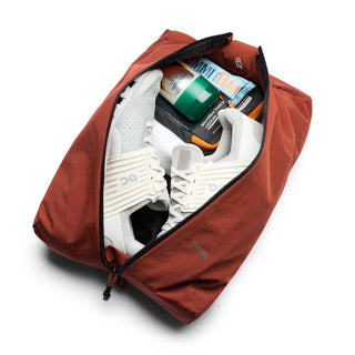 Bellroy Lite Packing Caddy 10L in rust color holding white sneakers and travel essentials inside