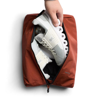 Bellroy Lite Packing Caddy 10L in rust color holding white gym shoes with smooth recycled nylon fabric