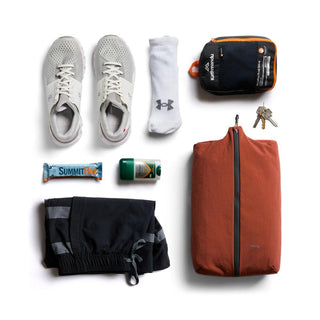 Bellroy Lite Packing Caddy 10L in rust with travel essentials including shoes, socks, and keys arranged nearby