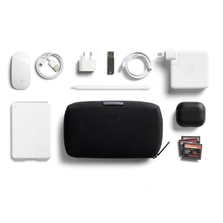Bellroy Tech Kit black fabric tech organizer pouch surrounded by chargers and accessories on white background