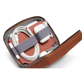Bellroy Tech Kit Compact in brown with organized cables and white earbuds secured by elastic straps