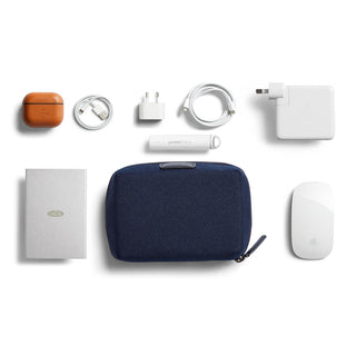 Bellroy Tech Kit Compact in navy blue fabric alongside electronic accessories and charger cables arranged neatly