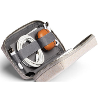 Bellroy Tech Kit Compact in light beige fabric with organized cables and earbuds inside the open case