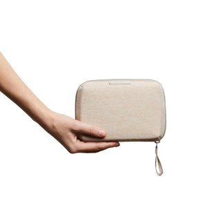 Bellroy Tech Kit Compact in beige fabric held by hand showing compact rectangular design with wrist strap
