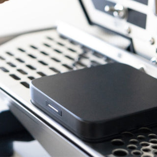 ACAIA Umbra Digital Scale resting on a metallic perforated surface with a sleek matte black finish