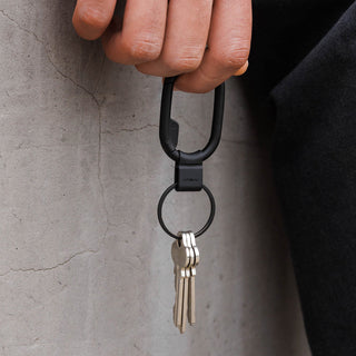 Orbitkey Clip Mini black zinc alloy key organizer attached to a carabiner holding three keys outdoors