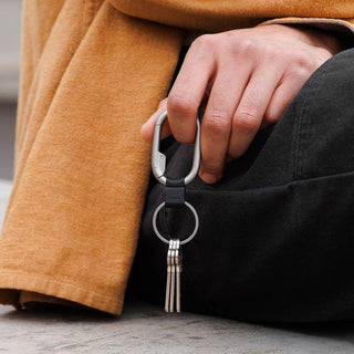 Orbitkey Clip Mini attached to keyring held by hand with keys, showcasing metal carabiner and black strap details