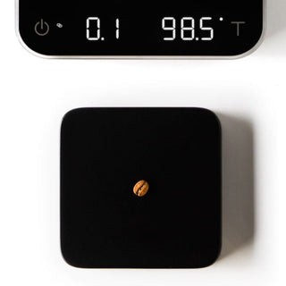 ACAIA Umbra Digital Scale in black with sleek surface weighing a single coffee bean under clear display panel