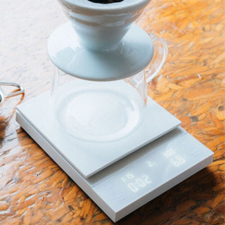 HARIO Polaris Coffee Scale with white acrylic platform weighing glass carafe on wooden surface