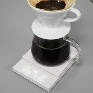 HARIO Polaris Coffee Scale in white with digital display weighing a glass carafe of brewed coffee